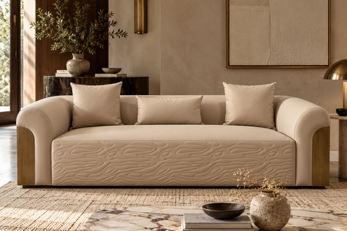 A cream-colored upholstered sofa with a textured wave pattern on the seat, styled in a warm, modern living room with a marble coffee table and neutral decor.