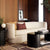 A cream bouclé sofa in a modern living room setting with wood-paneled walls, a patterned rug, a black coffee table, and accent pillows.