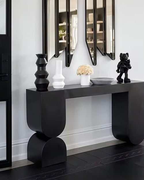 The Noir Console is a striking fusion of contemporary design and sculptural artistry. Crafted with clean lines and bold geometric shapes, it features a deep matte black finish that adds drama and sophistication to any interior. Its sleek form and strong presence make it a perfect statement piece for entryways, living rooms, or hallways where modern elegance and functional style are key.