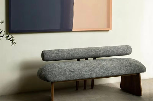 Modern upholstered bench featuring a soft curved seat, cylindrical backrest and sculptural wooden legs, designed for contemporary luxury interiors.