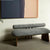 Modern upholstered bench featuring a soft curved seat, cylindrical backrest and sculptural wooden legs, designed for contemporary luxury interiors.