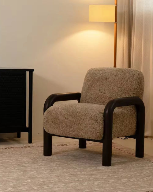 Rico Accent Chair featuring a warm textured upholstered seat and backrest, sculptural dark wooden curved arms, and a sturdy wooden frame with an architectural silhouette.